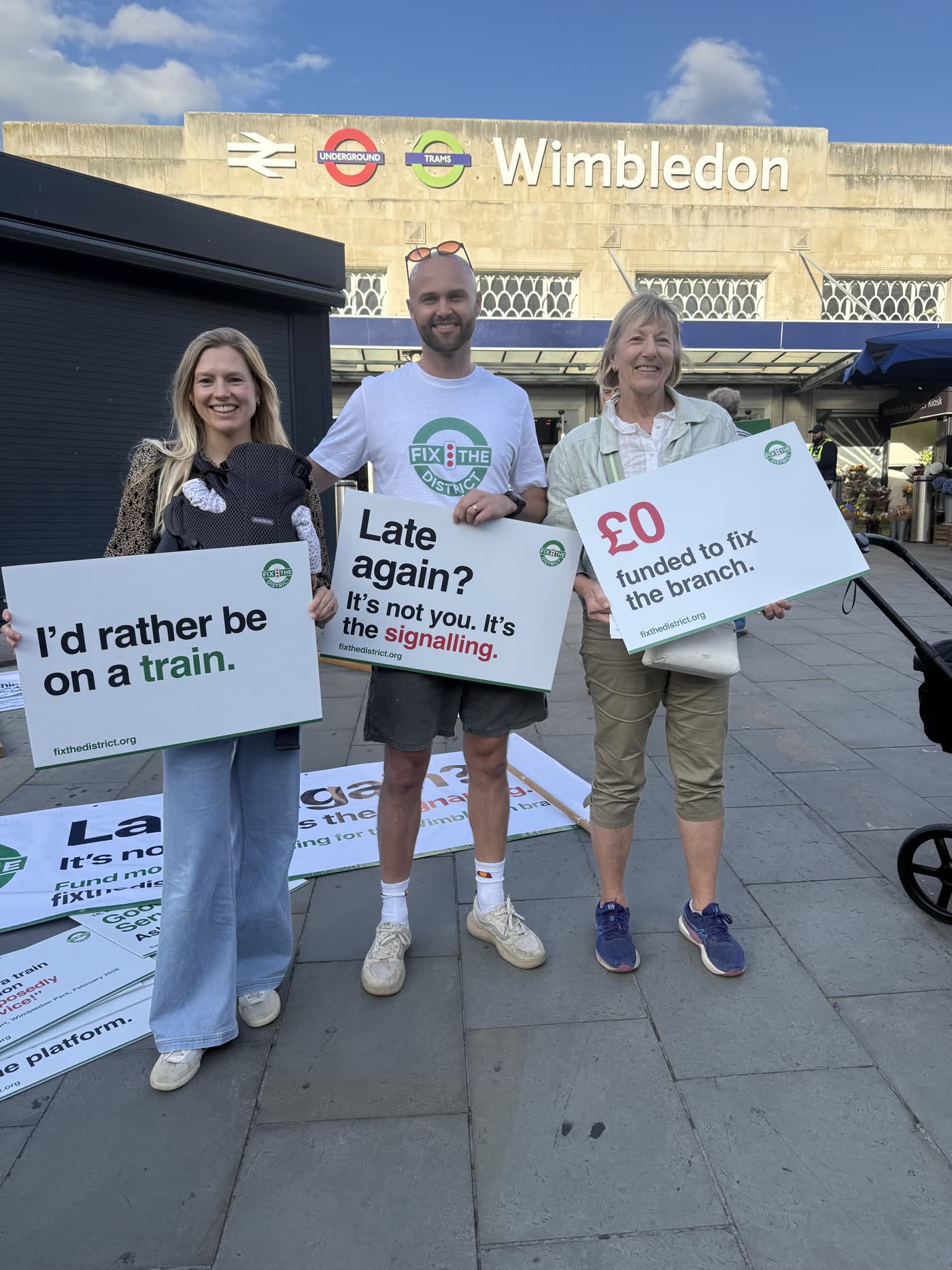 Three campaigners with placards reading “I’d rather be on a train.”, “Late again?” and “£0 funded to fix the branch.”